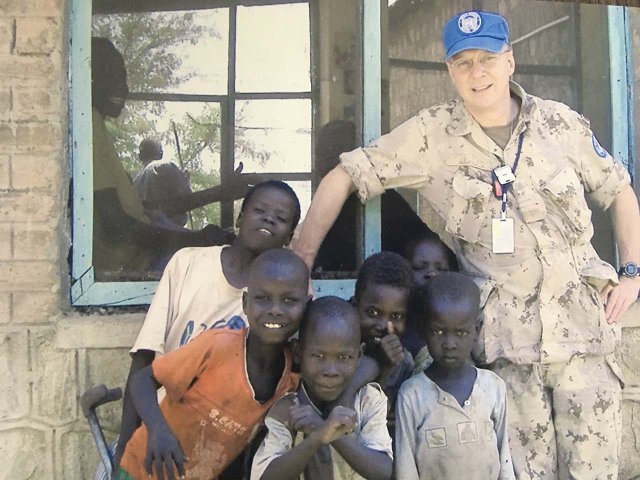 In Sudan in 2005, in addition to his job as a military observer, LCol Goodspeed voluntarily initiated a project to help orphaned children. The photo shows Michael in front of an orphanage in Juba with crippled and undernourished boys. On his own initiative Michael adopted the orphanage and succeeded in getting it registered as a “UN Quick Impact Project.” In war torn Sudan, orphaned boys were considered an unwelcome social burden and were rarely adopted and routinely overlooked by the country’s over-stressed and inadequate social services. Goodspeed organized UN engineers to repair their building and coordinated with NGOs and UN agencies to ensure these children were housed, fed, clothed, given medical care and rudimentary schooling.
