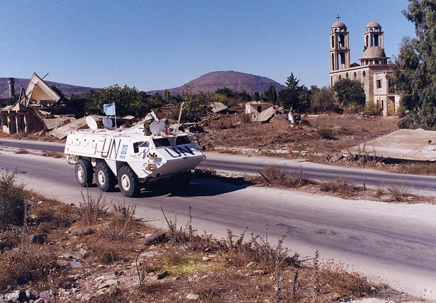 Un véhicule blindé de transport de troupes de la FNUOD du côté syrien à Quneitra. La colline à l'arrière-plan est occupée par les troupes juives des forces de défense israéliennes. L'église à droite est chrétienne. La ville était majoritairement musulmane. Il s'agit d'un exemple typique de la façon dont l'ONU opère dans le tourbillon des religions.